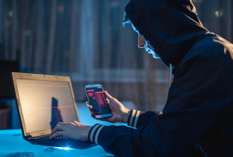 A person wearing a hoodie is busy working on a laptop computer. Cybersecurity practices for attorney. 